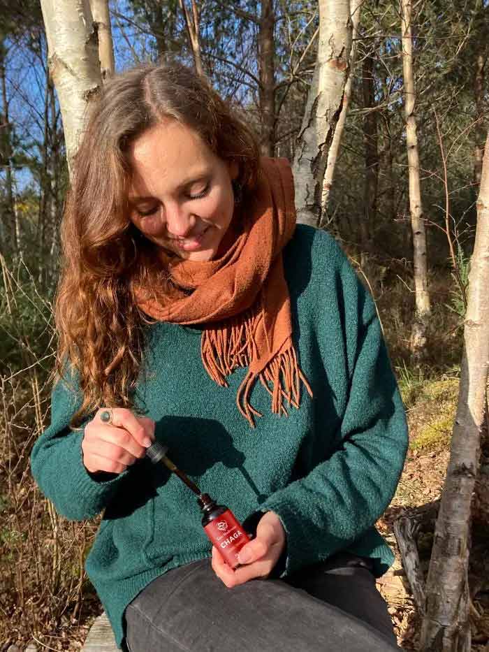 Woman in woods takes chaga tincture, symbolizing nature-wellness connection.